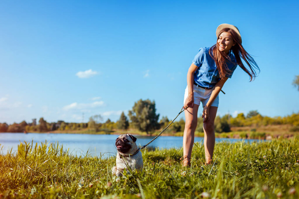 Pug dog sitting by river. Happy puppy waiting a command of master. Dog and woman chilling outdoors - 写真・画像