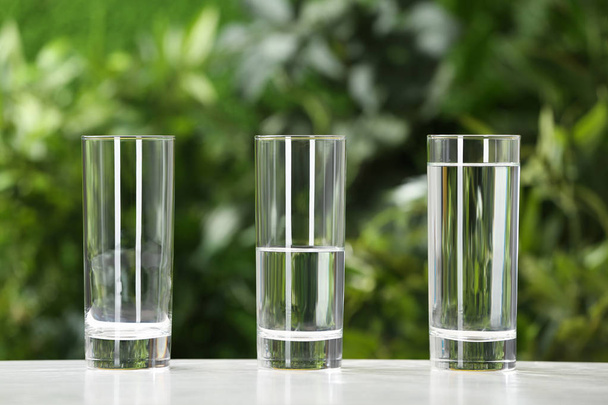 Empty, half and full glasses of water on white table against blurred background - Zdjęcie, obraz