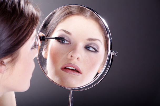 jonge vrouw in cosmetische spiegel kijken - Foto, afbeelding