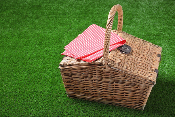 Toalha de mesa quadriculada e cesta de piquenique de vime fechada na grama verde, espaço para texto
 - Foto, Imagem