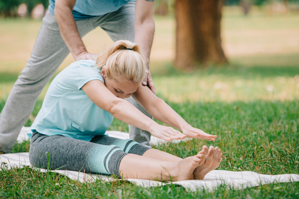 cropped view of man helping woman practicing yoga pose in park - Foto, imagen