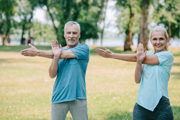 smiling mature man and woman exercising in park together and smiling at camera - Foto, Imagem