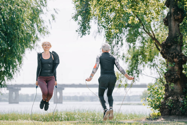 взрослый спортсмен и спортсменка тренируются с скакалками в парке
 - Фото, изображение