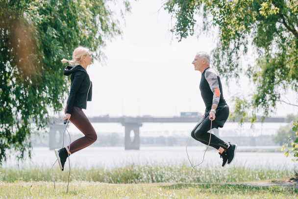 side view of mature sportsman and sportswoman training with jump ropes in park together - Photo, Image