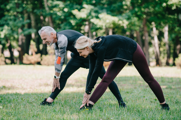 positiver, reifer Sportler und Sportlerin beim gemeinsamen Stretching im Park  - Foto, Bild