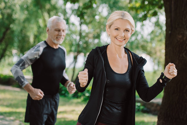 cheerful mature sportsman and sportswoman jogging in park together - Foto, imagen