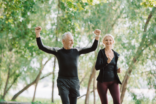 cheerful mature sportsman showing yes gesture while running near smiling sportswoman - Photo, Image