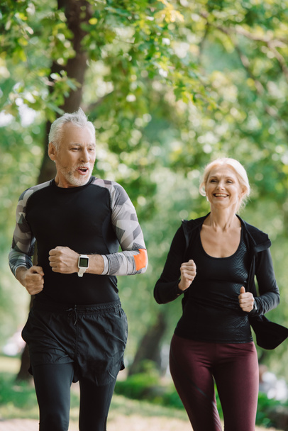cheerful mature sportsman and sportswoman running together in park - Фото, зображення