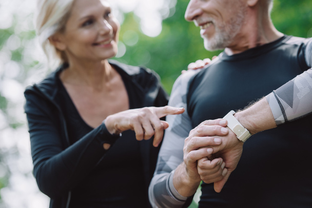 selective focus of smiling sportswoman pointing at smart watch on hand of mature sportsman - Fotoğraf, Görsel
