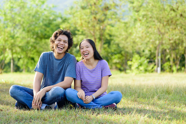 feliz asiático pareja riendo y sentado en verde hierba en al aire libre
 - Foto, Imagen