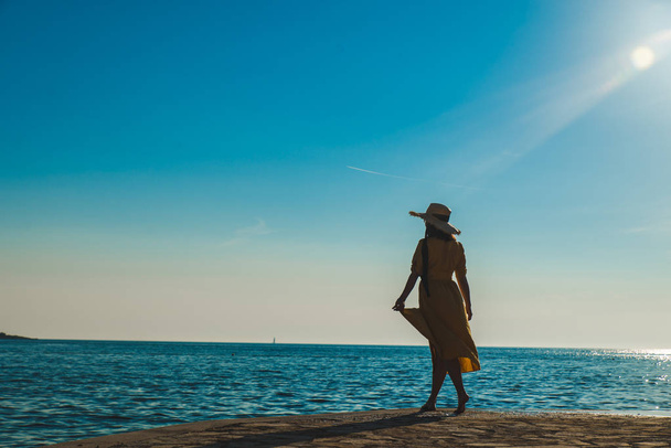 Młoda Ładna uśmiechnięta kobieta w żółtym sundress spaceru po kamiennej plaży - Zdjęcie, obraz