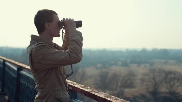 Young man with red hair in in khaki coat looking through binoculars from the bridge. - Footage, Video