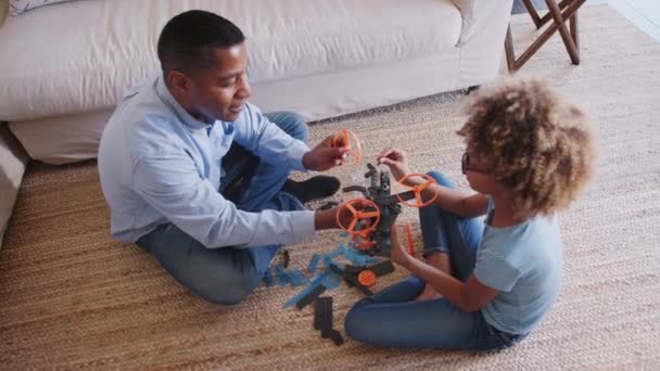 Pre-teen African American girl and grandad sitting cross legged on the floor constructing a toy, elevated view - Filmmaterial, Video