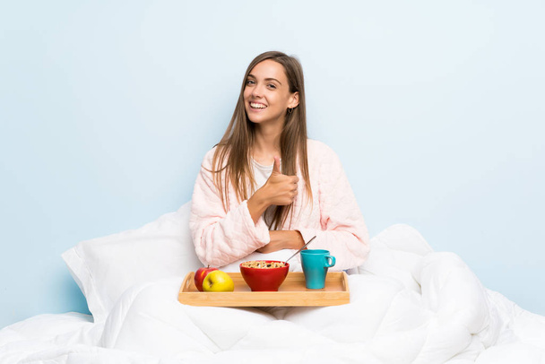 Молодая женщина в халате с завтраком подает большой палец вверх жестом
 - Фото, изображение