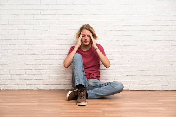 Hombre rubio sentado en el suelo con dolor de cabeza
 - Foto, Imagen