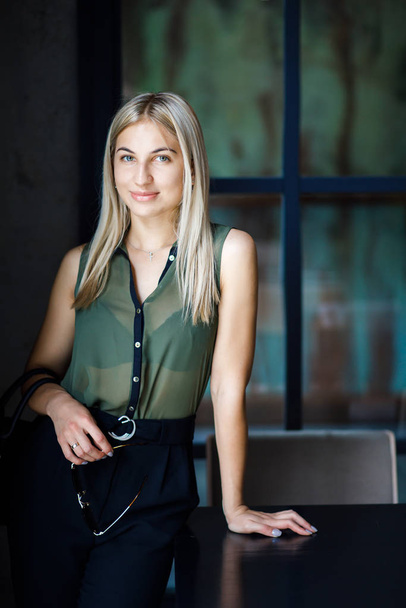A young beautiful blonde girl stands in a cafe with a bag in her arms. The girl is well dressed, business style. The girl is ready for a business meeting - Foto, immagini