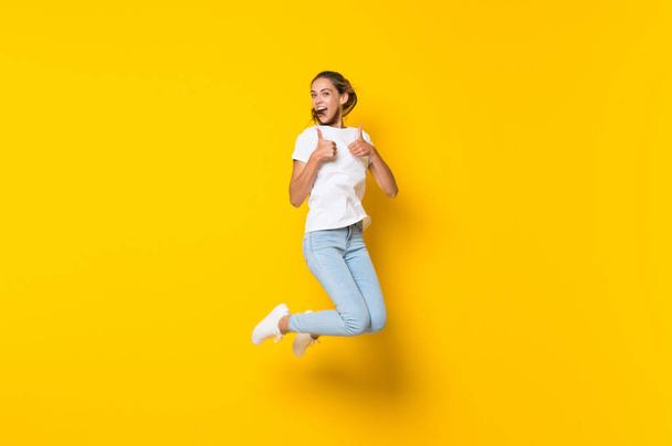 Young woman jumping over isolated yellow wall - Fotoğraf, Görsel