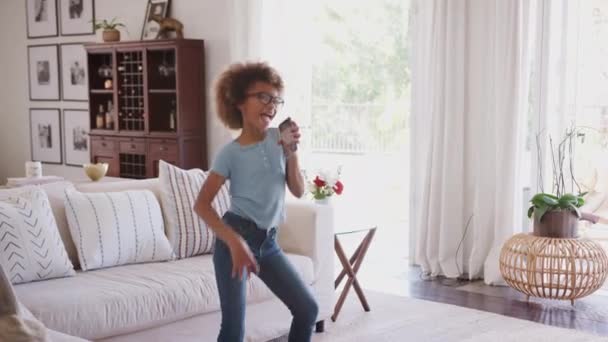 Pre-adolescente chica afroamericana bailando y cantando en casa usando el teléfono como un micrófono, de tres cuartos de longitud
 - Imágenes, Vídeo