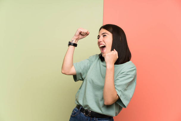 Jonge vrouw over geïsoleerde kleurrijke muur vieren een overwinning - Foto, afbeelding