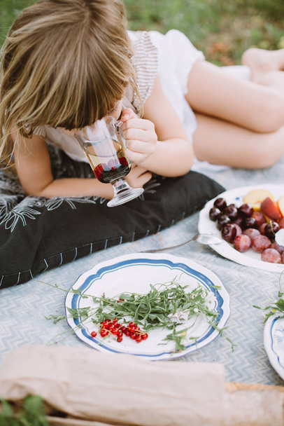 庭の毛布の上に横たわっているベリーとお茶を飲む小さな女の子 - 写真・画像