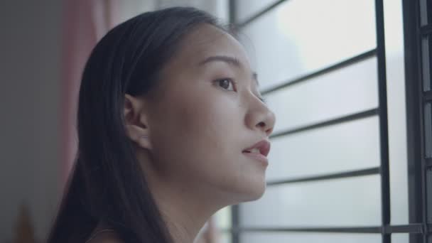 Close-up portret glimlachende Aziatische vrouw opening gordijnen in de kamer thuis kijkt uit het raam in de ochtend vakantie tijd. - Video