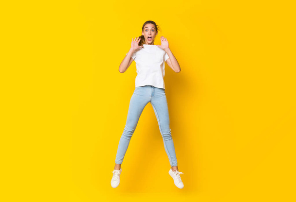 Young woman jumping over isolated yellow wall - Photo, Image