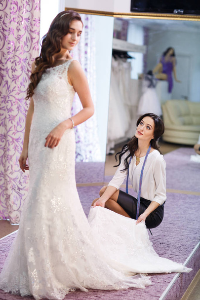 Female trying on wedding dress in a shop with women assistant. - Foto, Imagem