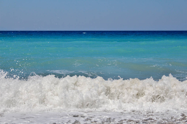 海岸に打ち寄せる泡立つ波と澄んだ青空を持つ青い海の色合い - 写真・画像