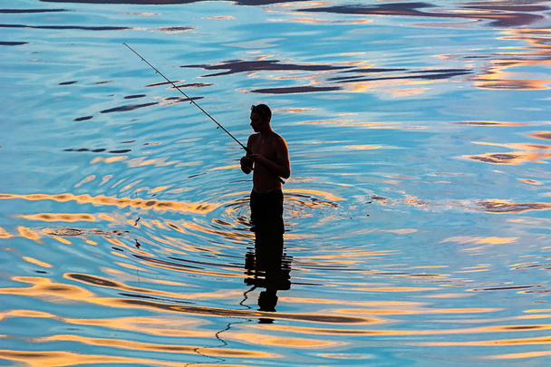 silhueta de um pescador em reflexão em ondulações de água
  - Foto, Imagem