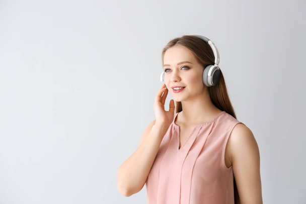 Beautiful young woman listening to music on light background - Фото, зображення