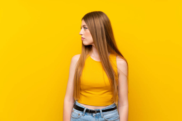 Jonge vrouw over geïsoleerde gele achtergrond uitziende kant - Foto, afbeelding