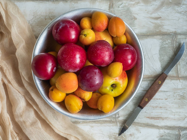 Full plate of ripe fresh apricot fruit, nectarine and plum close-up on a light wooden table, top view. Knife with wooden handle for cutting fruit. Soft cream cloth - Foto, immagini
