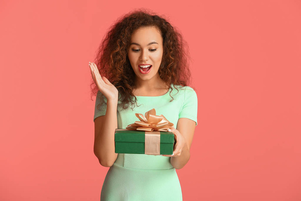 Здивована молода жінка з подарунком на кольоровому фоні
 - Фото, зображення