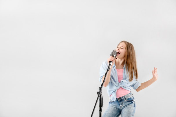 Εφηβικό κορίτσι με μικρόφωνο τραγουδώντας ενάντια στο φως φόντο - Φωτογραφία, εικόνα
