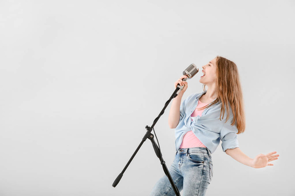 Teenage girl with microphone singing against light background - 写真・画像
