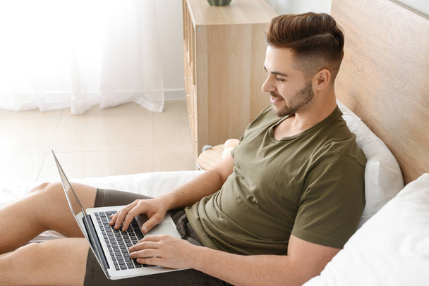 Όμορφος άνθρωπος με φορητό υπολογιστή που αναπαύεται στο υπνοδωμάτιο - Φωτογραφία, εικόνα