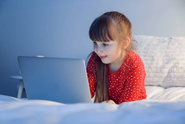 Cute little girl using laptop in bed at night - Foto, afbeelding