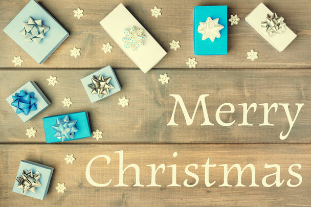 Χριστουγεννιάτικη σύνθεση με την επιγραφή καλά Χριστούγεννα. Λευκά και μπλε κουτιά δώρων διακοσμημένα με τόξα. Εορταστική διάταξη. - Φωτογραφία, εικόνα