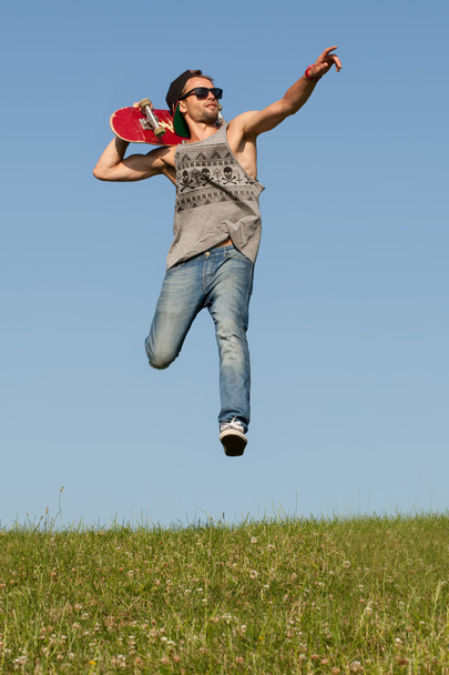Homem com um skate apontando e saltando
 - Foto, Imagem