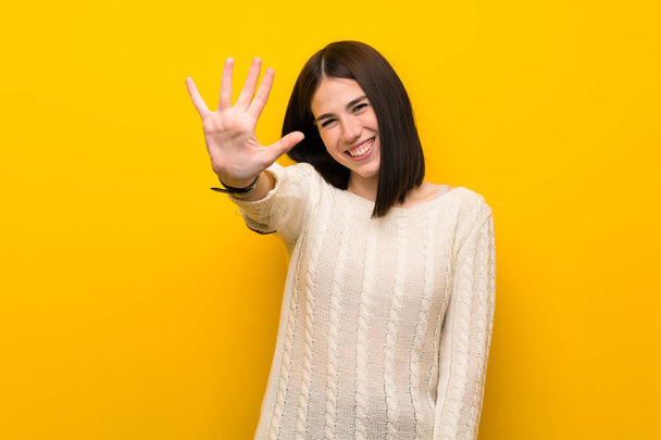 孤立した黄色い壁の上の若い女性は指で5を数える - 写真・画像