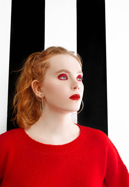 portrait of beautiful young redhead woman with stylish make up and in red sweater on black and white background - Photo, Image