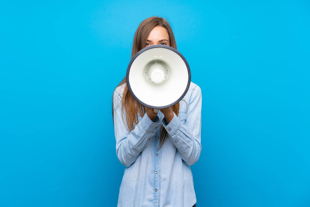 Mladá žena na izolovaném modrém pozadí křičící přes megafon - Fotografie, Obrázek