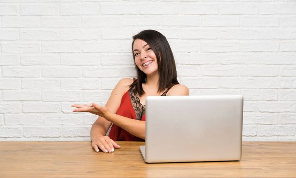 Young Mexican woman with a laptop extending hands to the side for inviting to come - Photo, Image