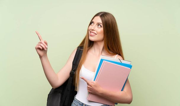 Fiatal diák nő több mint elszigetelt zöld háttérrel mutat a mutatóujját egy nagy ötlet - Fotó, kép