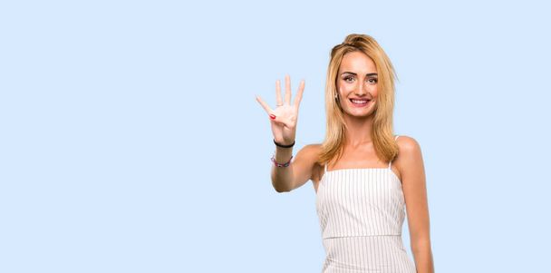 Young blonde woman happy and counting four with fingers over isolated blue background - Photo, image