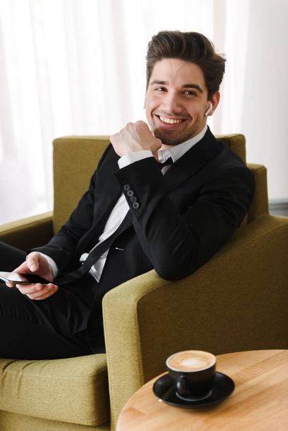 Confident handsome man wearing suit sitting in armchair - Foto, afbeelding