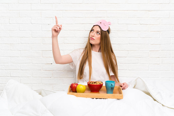 Молодая женщина в халате с завтраком указывает назад указательным пальцем
 - Фото, изображение