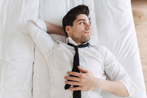 Photo from top of caucasian bearded businessman lying on bed in hotel apartment - Photo, Image