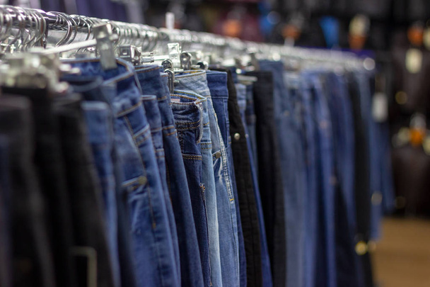 Wiele różnych niebieskie dżinsy na wieszaku wiszącego w sklepie ubrania sklep. Miękkie selektywne fotografowanie ostrości - Zdjęcie, obraz