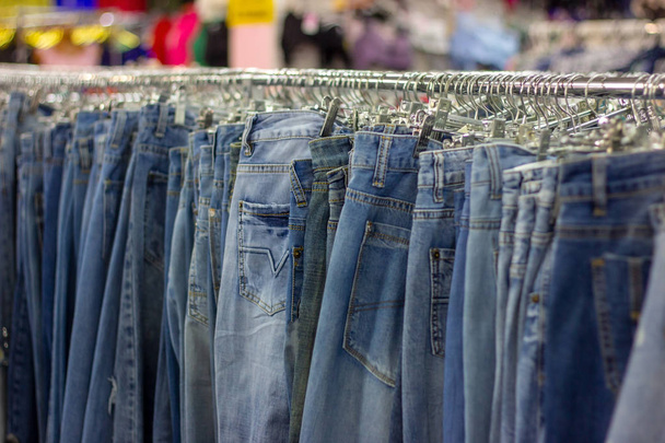 Many different blue Jeans on a hanging rack in the clothes shop store. Soft selective focus photography - Photo, Image